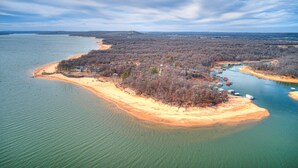 Vista aérea de una zona costera con una playa arenosa, una pequeña isla con edificios y barcos en el agua.