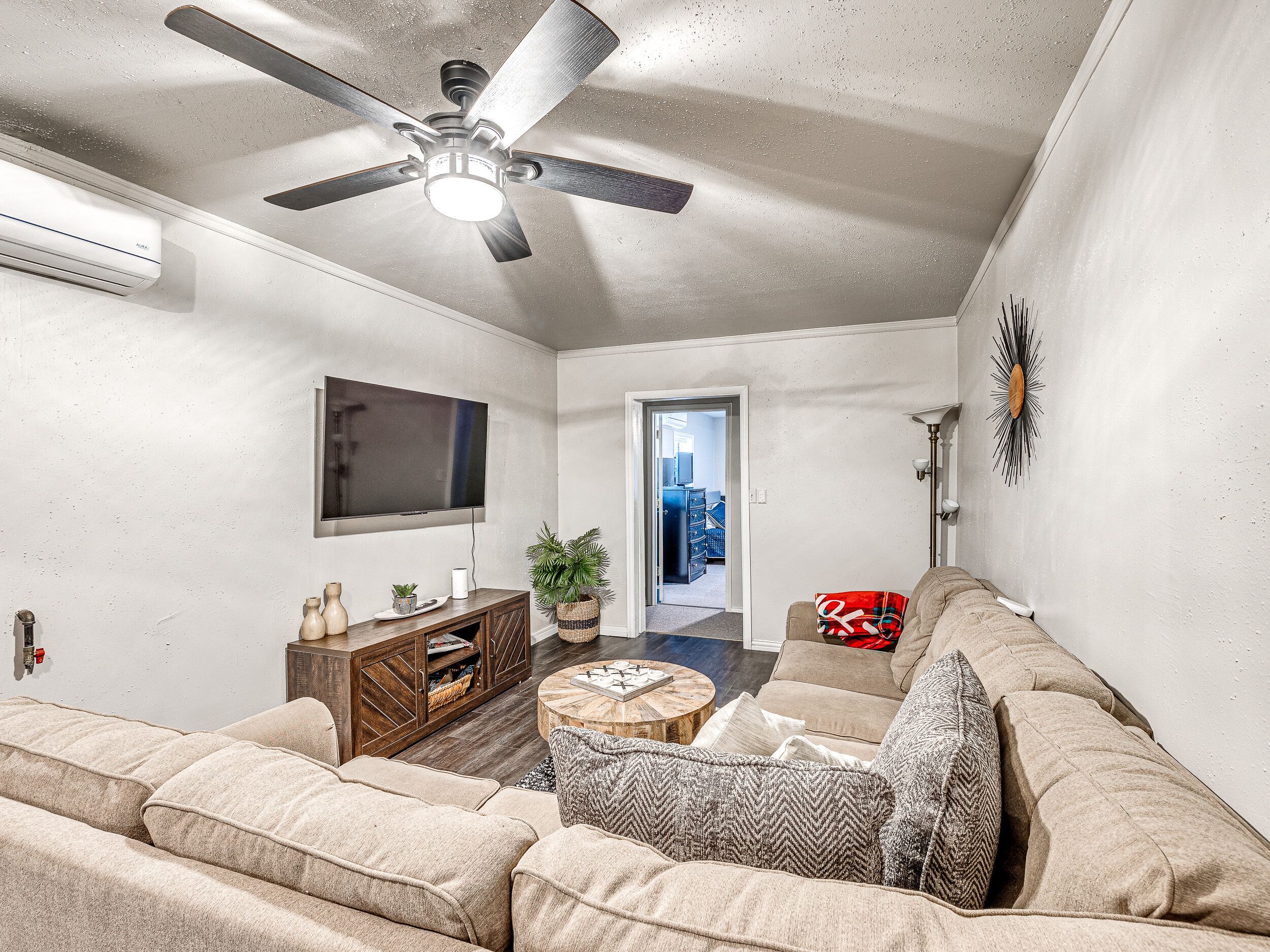 A living room with a ceiling fan, a flat-screen TV, a wooden entertainment unit, a beige sofa, and a coffee table.