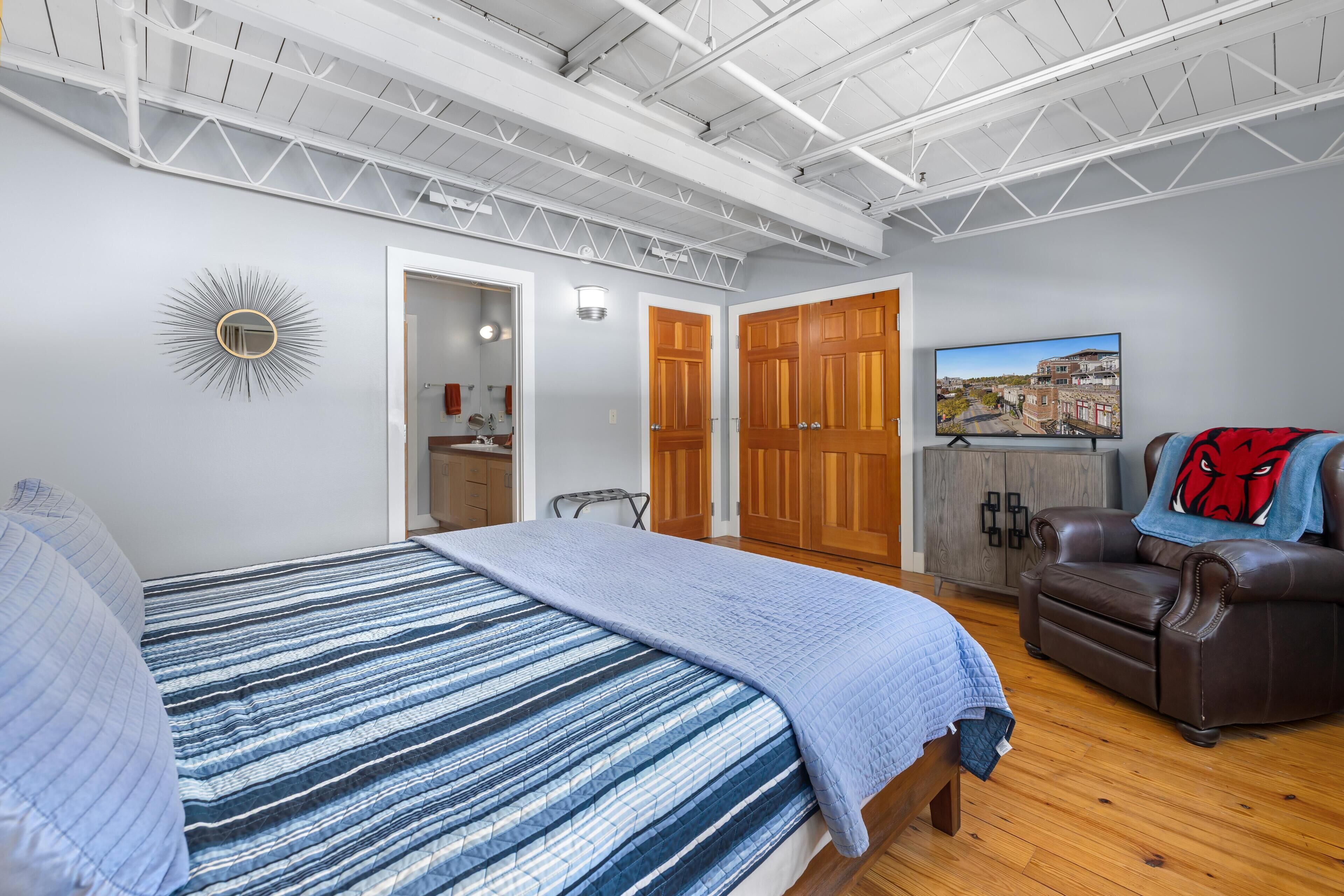 A bedroom with a bed, a chair, a TV, and a couch.