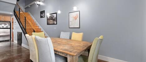 Un comedor con una mesa y sillas de madera, una escalera y obras de arte en las paredes.