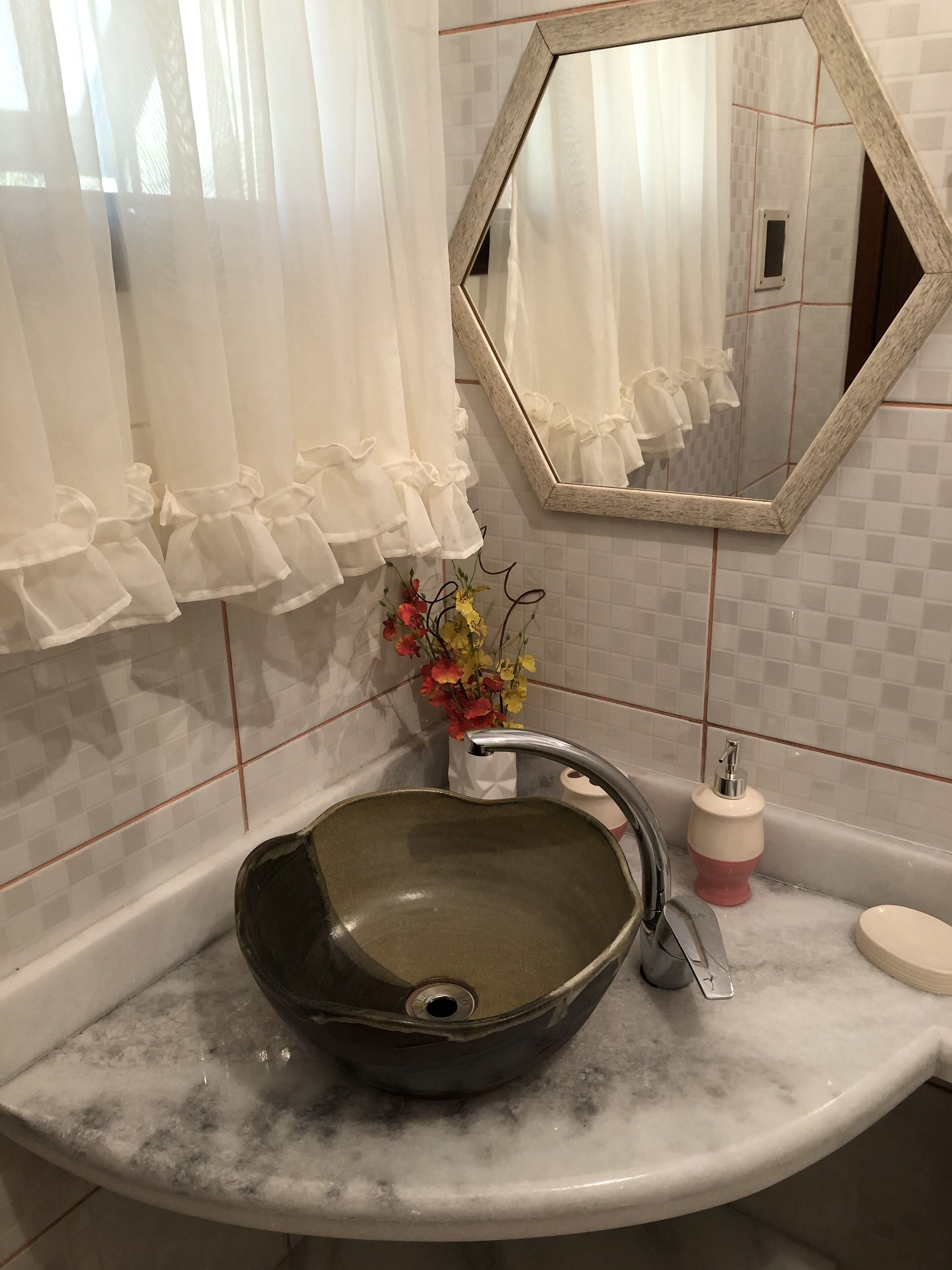 A bathroom with a marble sink, a mirror, and a vase with flowers.