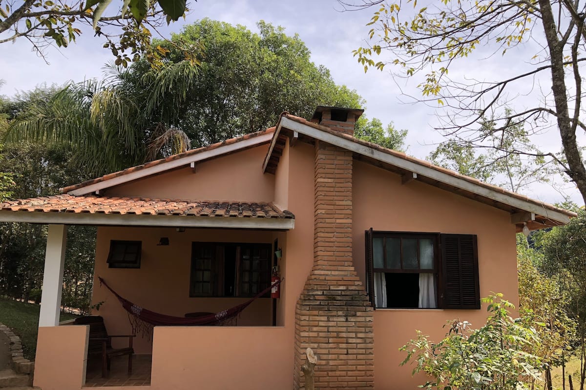 Una casa de un piso con techo de tejas, una chimenea de ladrillo y un porche con una hamaca.