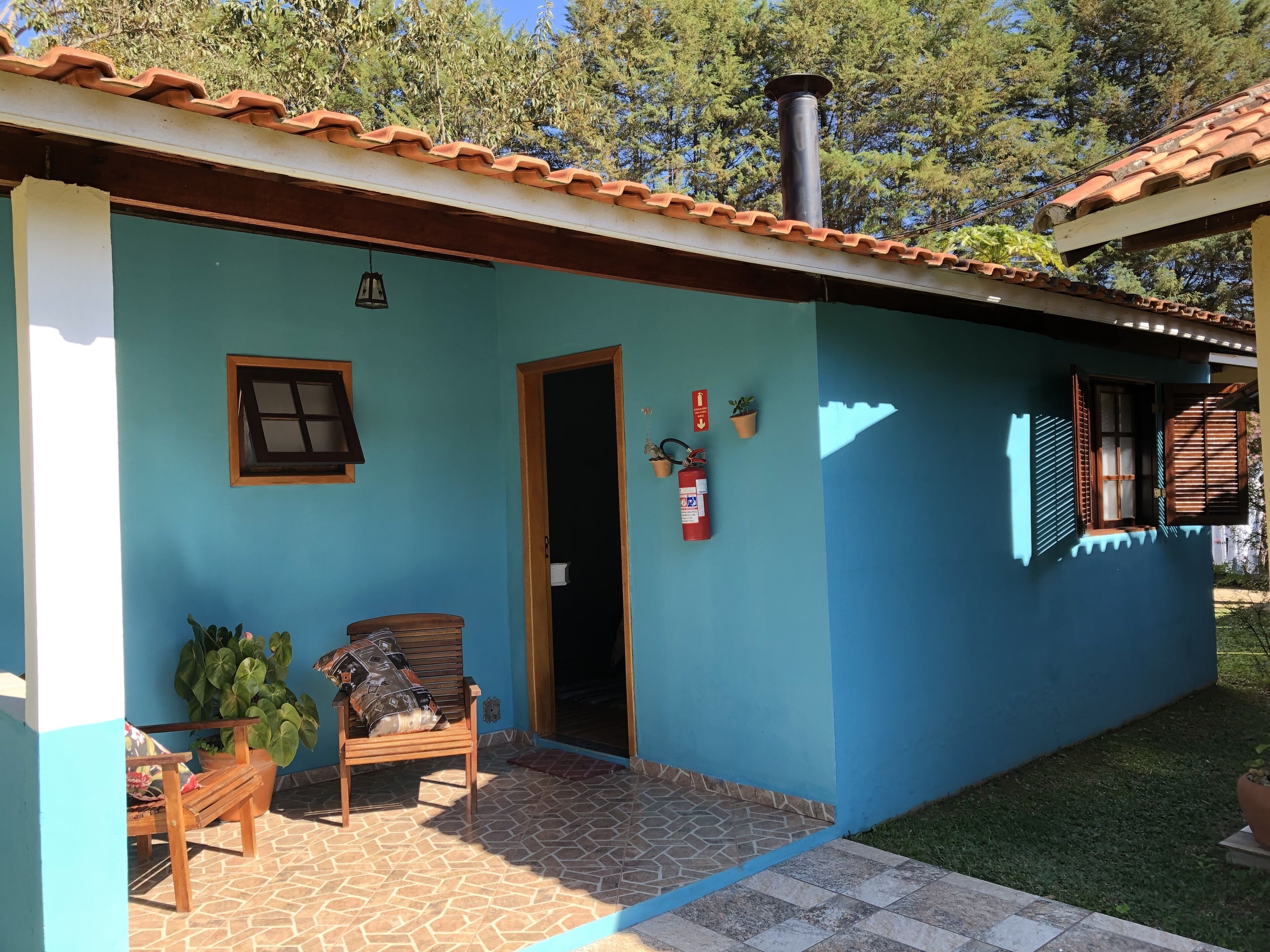 A house with a tiled porch, a wooden bench, a fire extinguisher, and a chimney.