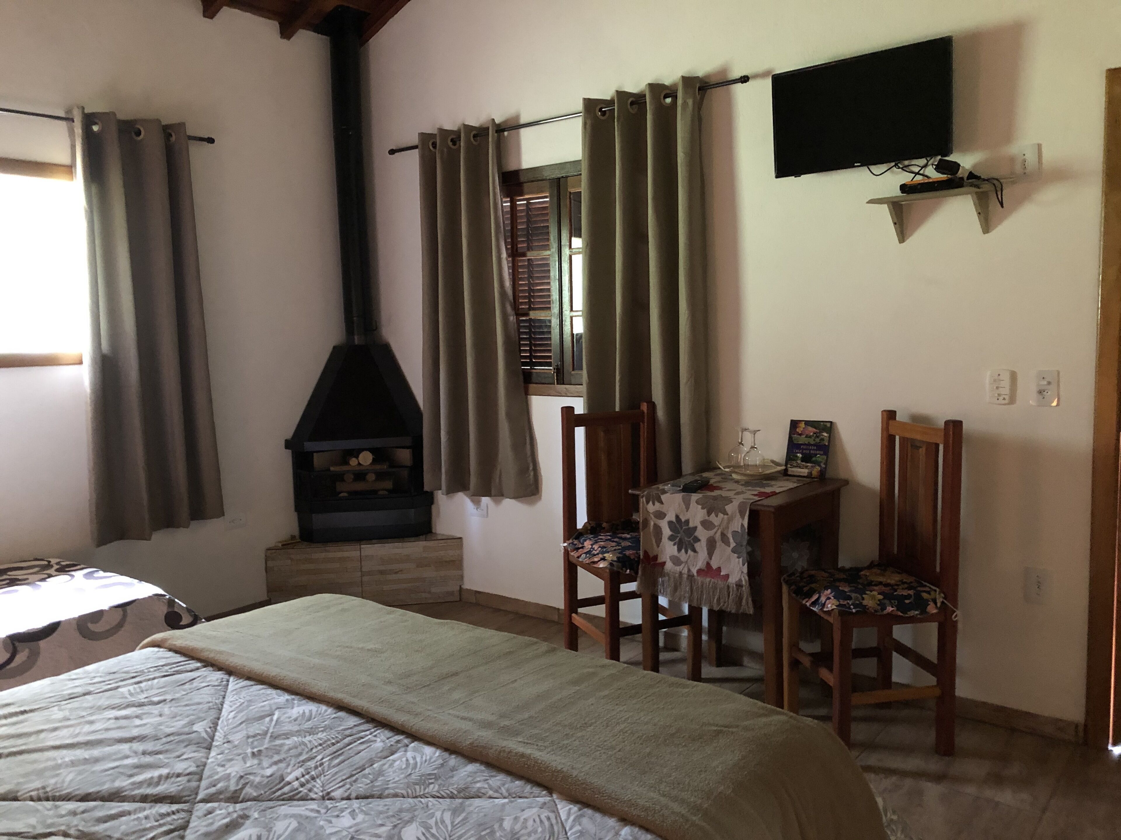 A bedroom with a bed, a wooden table with chairs, a fireplace, and a television on the wall.