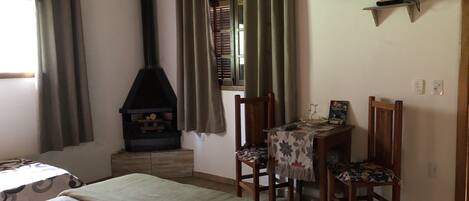 A bedroom with a bed, a wooden table with chairs, a fireplace, and a television on the wall.