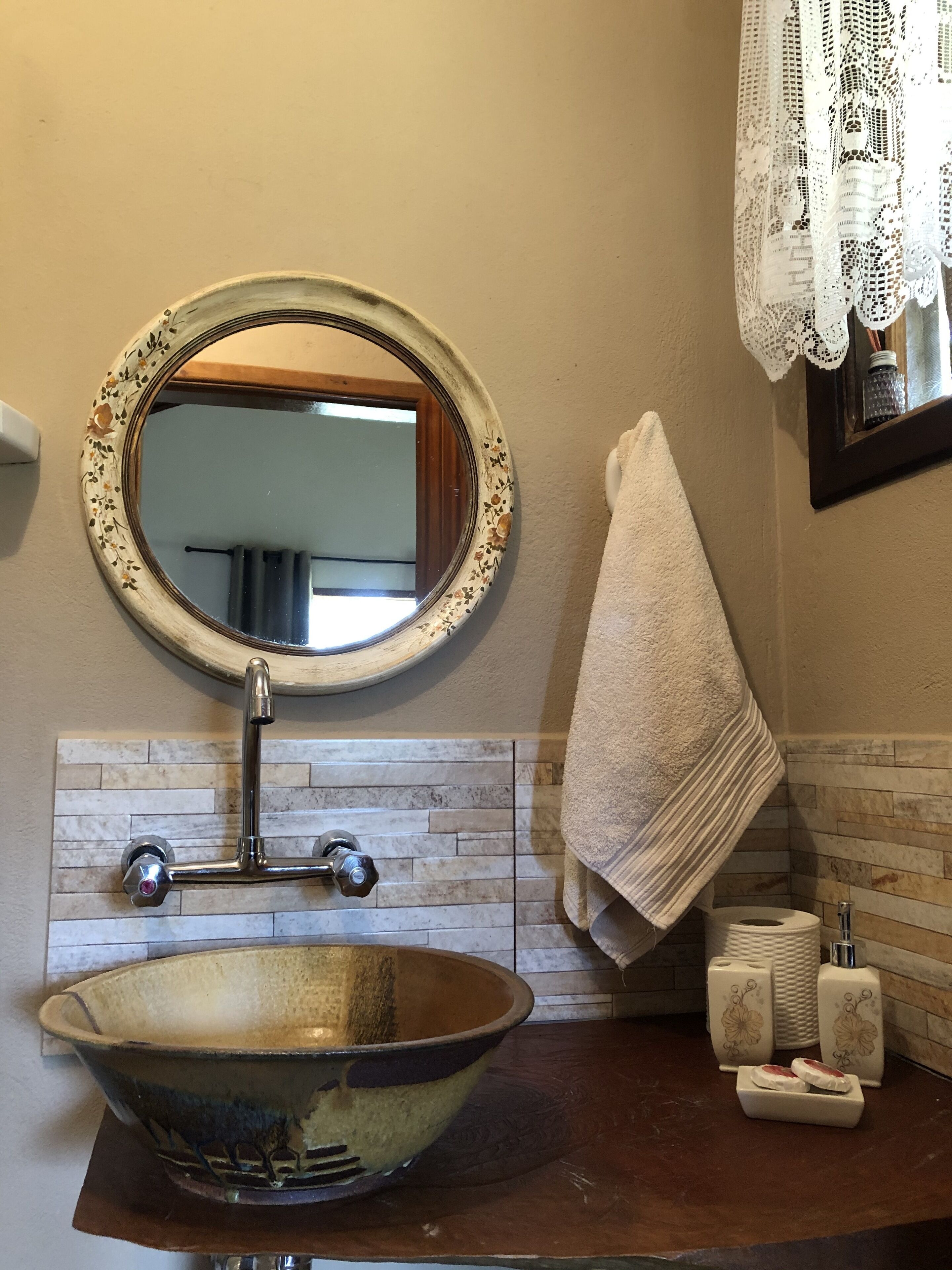 A bathroom with a round mirror, a ceramic sink, a towel, and a soap dispenser.