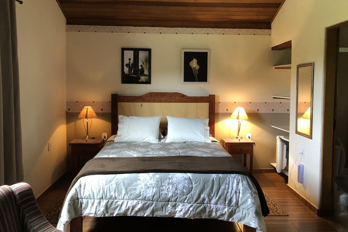 Un dormitorio con techo de madera, una cama con edredón blanco, dos lámparas de pared y dos cuadros enmarcados.