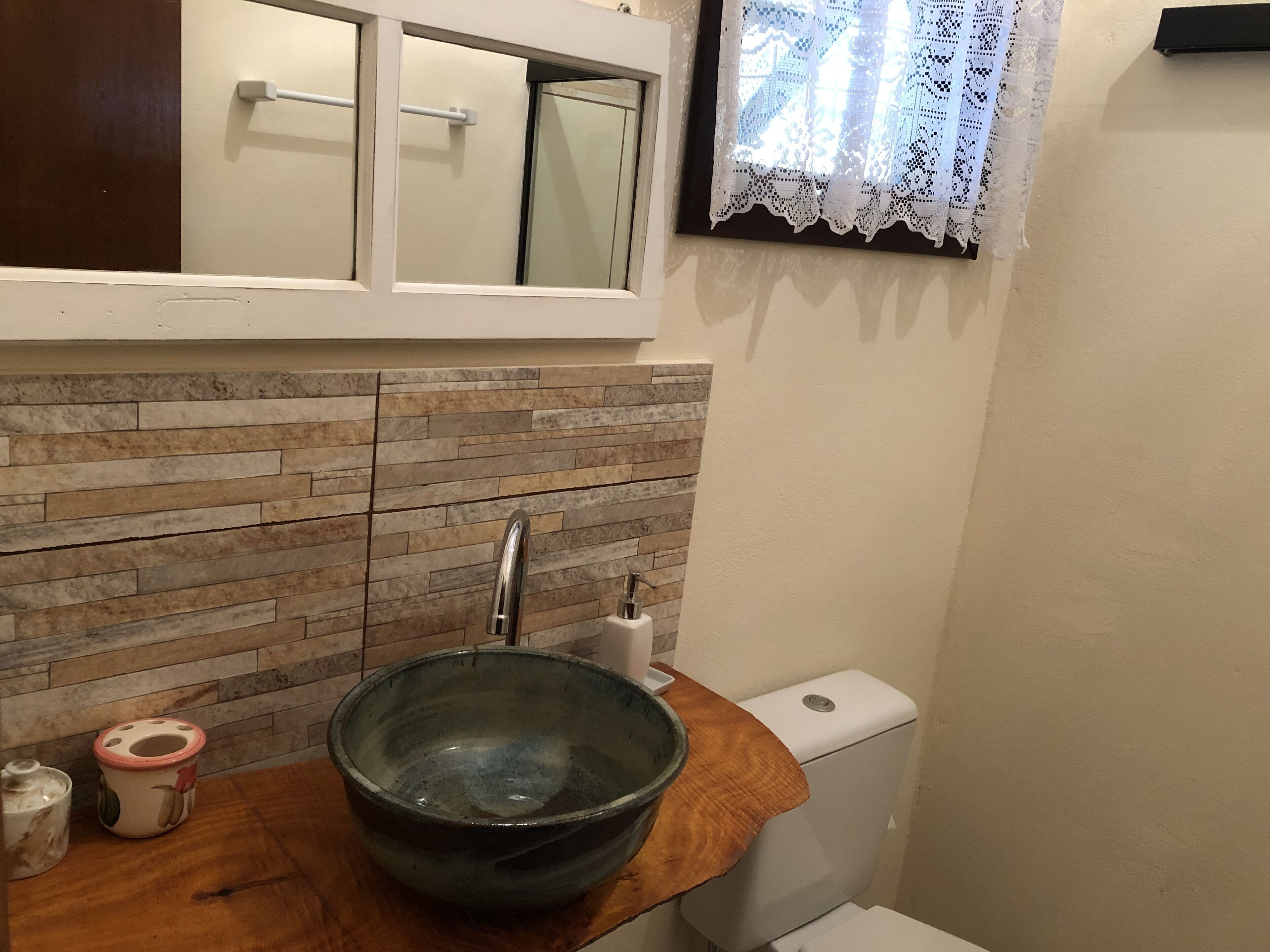 Un baño con salpicadero de piedra, encimera de madera, un lavabo de cerámica grande, inodoro y espejo sobre el lavabo.