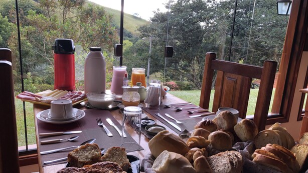 Una mesa de desayuno con diversos alimentos y bebidas, frente a una vista panorámica al aire libre.