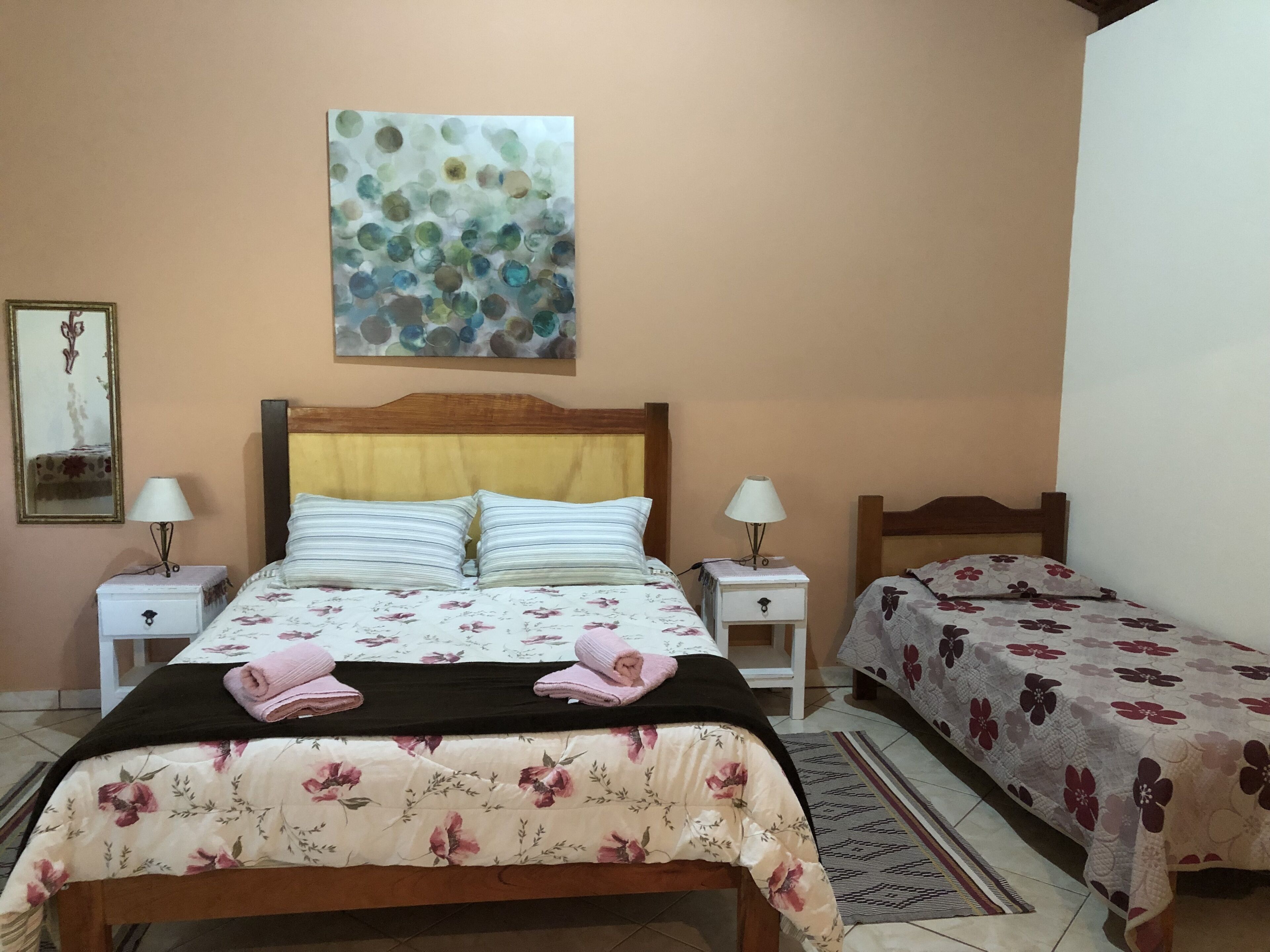 A bedroom with a bed, two bedside tables, a nightstand, a mirror, and a wall art piece.