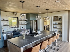 Una cocina moderna con una isla grande, taburetes de bar, electrodomésticos de acero inoxidable e iluminación decorativa.