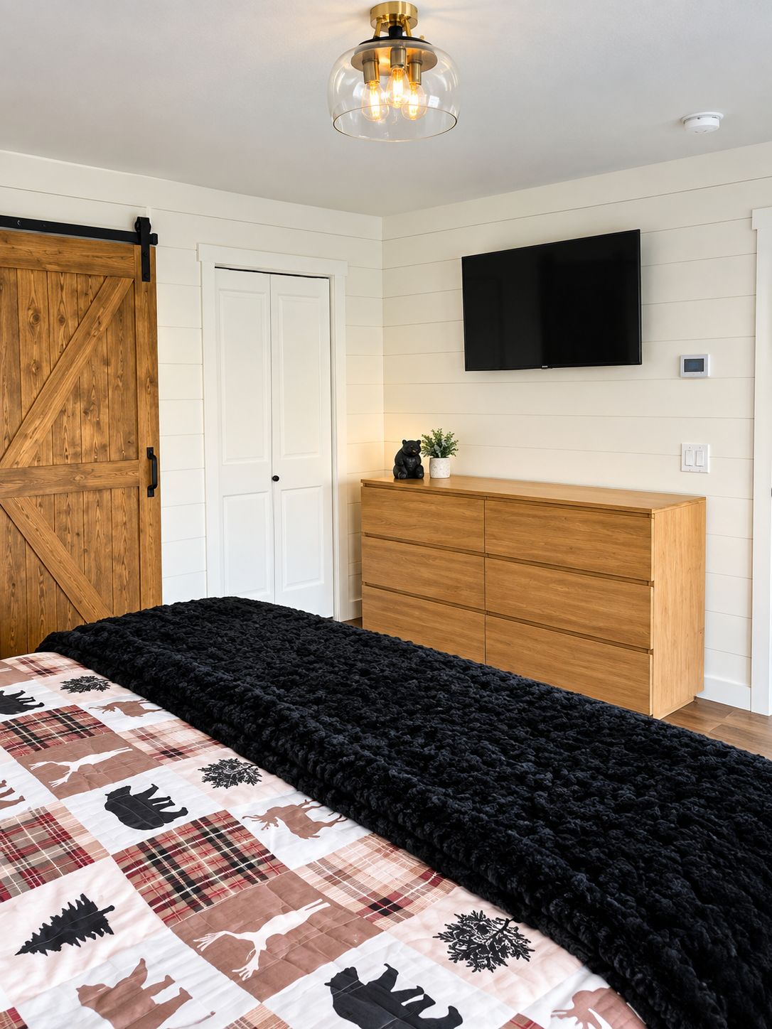 A bedroom with a large bed, a wooden wardrobe, a mounted TV, and a sliding barn-style door.