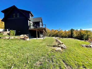 A two-story house with a balcony, surrounded by a grassy yard and a rocky area. - MegaVista Mountain Lodge - HGTV - Featured Retreat in the White Mountains.  (Intervale)