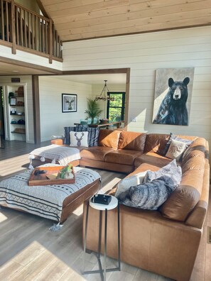A spacious living room with a large brown leather sofa, a wooden coffee table, and a dining area with a green table and chairs.