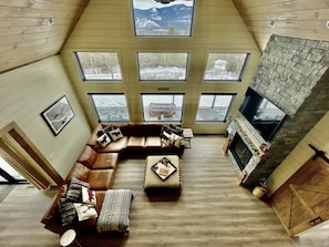 Una sala de estar tipo loft con un amplio sofá modular, varios ventanales, una chimenea de piedra y un televisor montado.