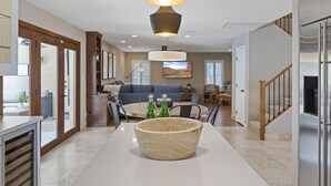 Una cocina moderna con una isla central, un comedor con mesa redonda y una sala de estar con sofá y un ventanal grande.