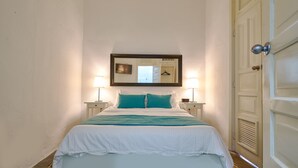 Ein ordentlich bezogenes Bett mit weißer und türkiser Bettwäsche, zwei Nachttischlampen und ein Spiegel über dem Bett.