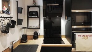 Cozinha moderna com bancada preta, cafeteira, chaleira e torradeira. Há um forno preto e micro-ondas sobre a bancada.