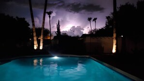 Una piscina al anochecer con palmeras y un cielo nublado.
