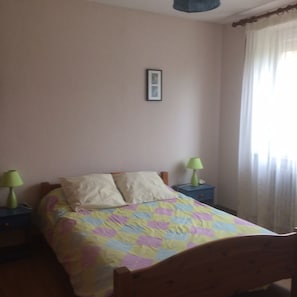 A bedroom with a bed, two bedside tables, a lamp on each, a framed picture on the wall, and a window with curtains.