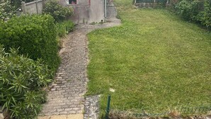 Un escalier en pierre mène à une petite construction en béton, entourée d’une zone herbeuse et d’un mur de briques.