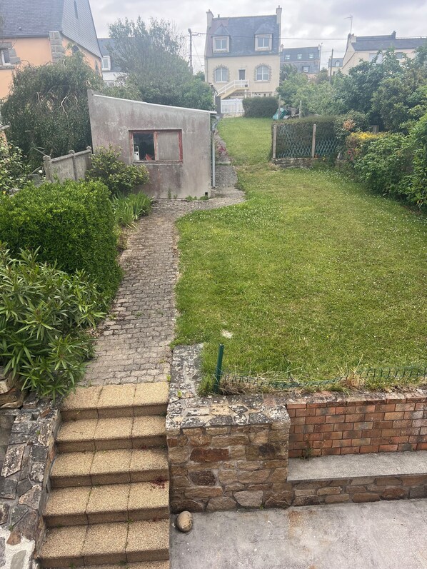 A stone staircase leading to a small concrete structure, surrounded by a grassy area and a brick wall.