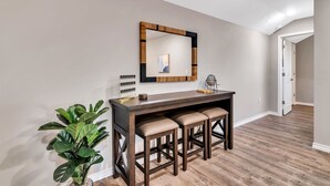 Een hal met een houten bureau, drie krukken, een spiegel en een plant in een pot.