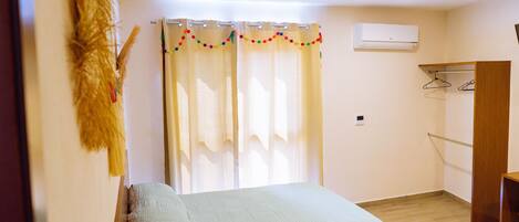 A room with two beds, a wooden wardrobe, a coat rack, and a window with curtains.