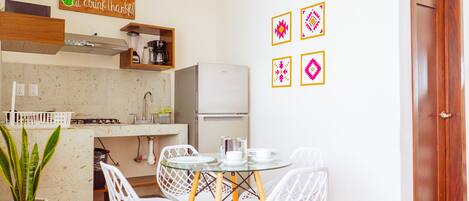 A compact kitchen with a dining area, white chairs, a small refrigerator, and a coffee machine.