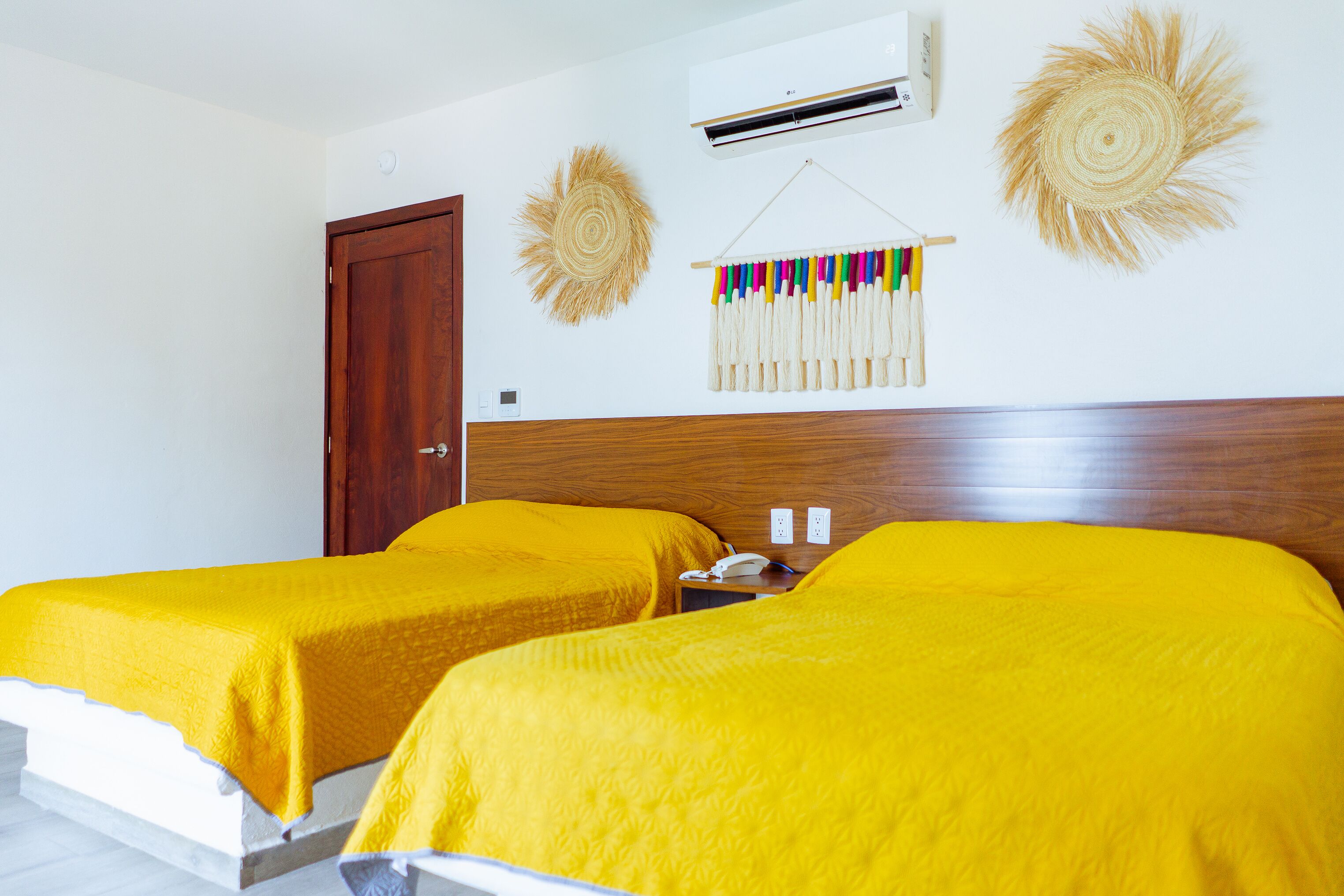 A hotel room with two beds, a wooden headboard, an air conditioning unit, and wall decorations.