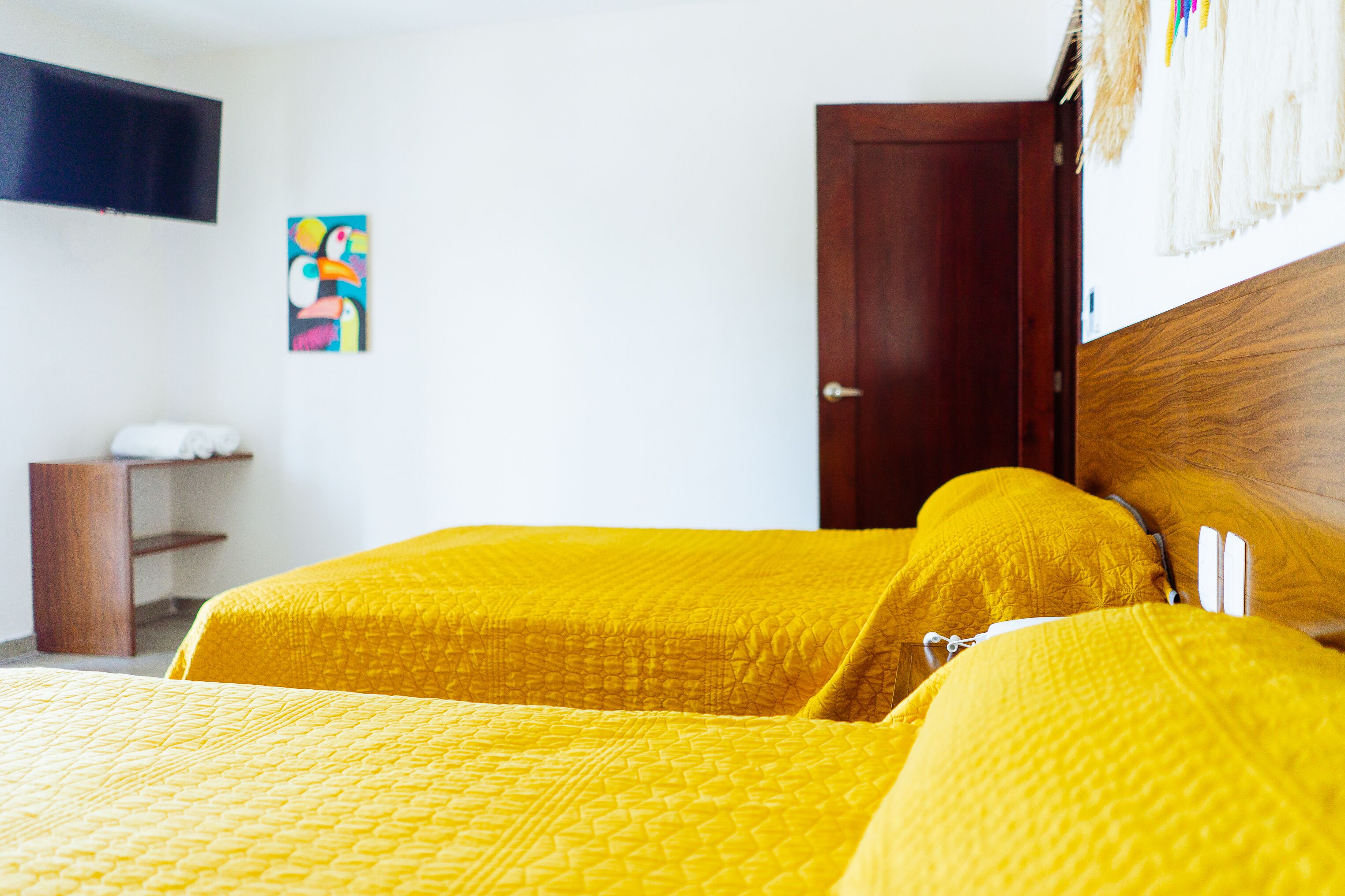 A room with a bed, a wooden headboard, a television mounted on the wall, and a colorful painting.