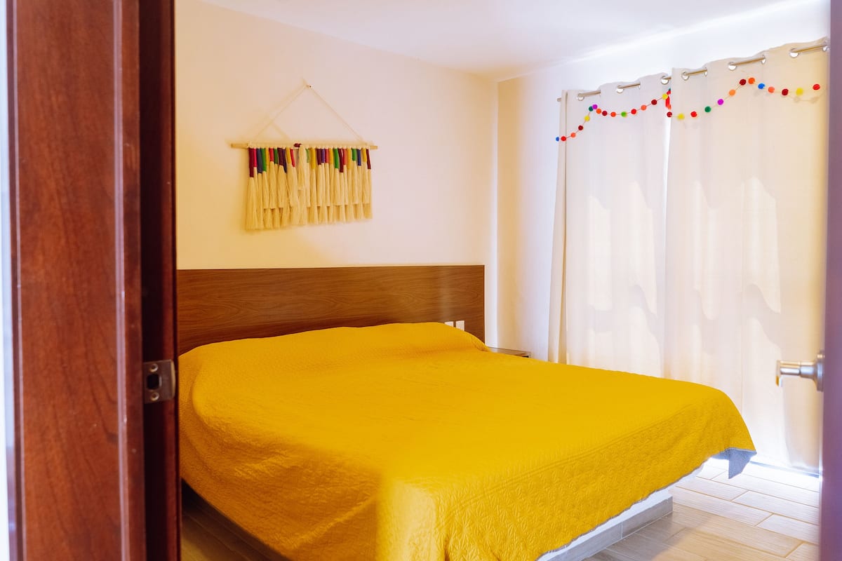 A room with a bed, wooden headboard, and a curtain with colorful tassels.