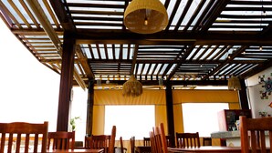 Un restaurante con mesas y sillas de madera, techo con vigas de madera y luces colgantes.