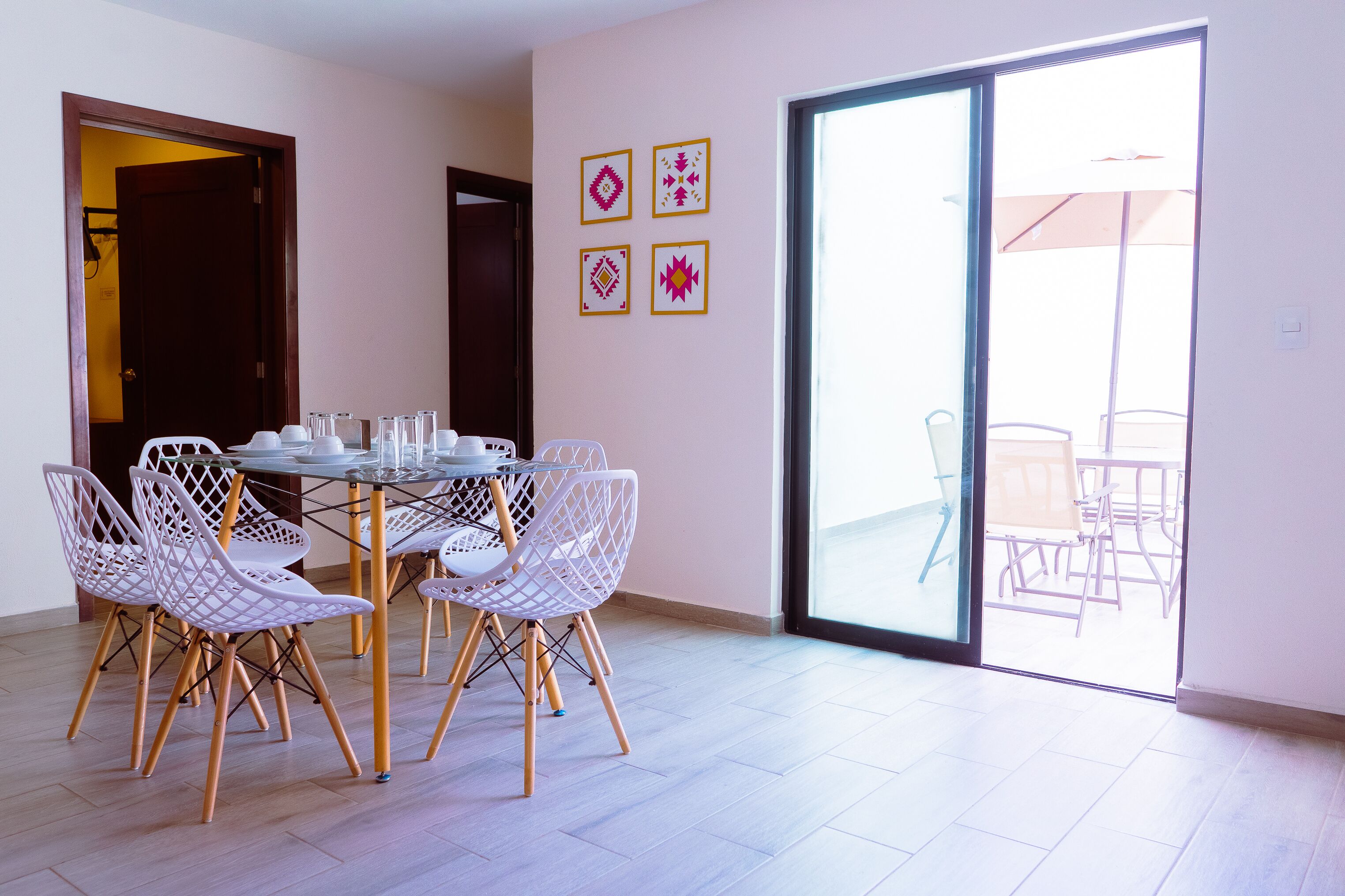 Un coin repas comprenant une table ronde et quatre chaises, une porte-fenêtre coulissante donnant sur un patio extérieur, et quatre éléments de décoration encadrés accrochés au mur.