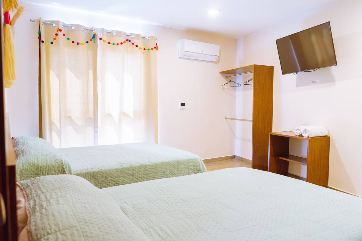 A hotel room with two beds, a wardrobe, a TV, and a window with curtains.
