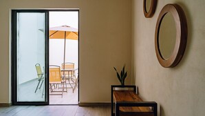 Una habitación con puerta corrediza de vidrio que da a un espacio exterior con mesa y sillas, un banco de madera y dos espejos fijados a la pared.