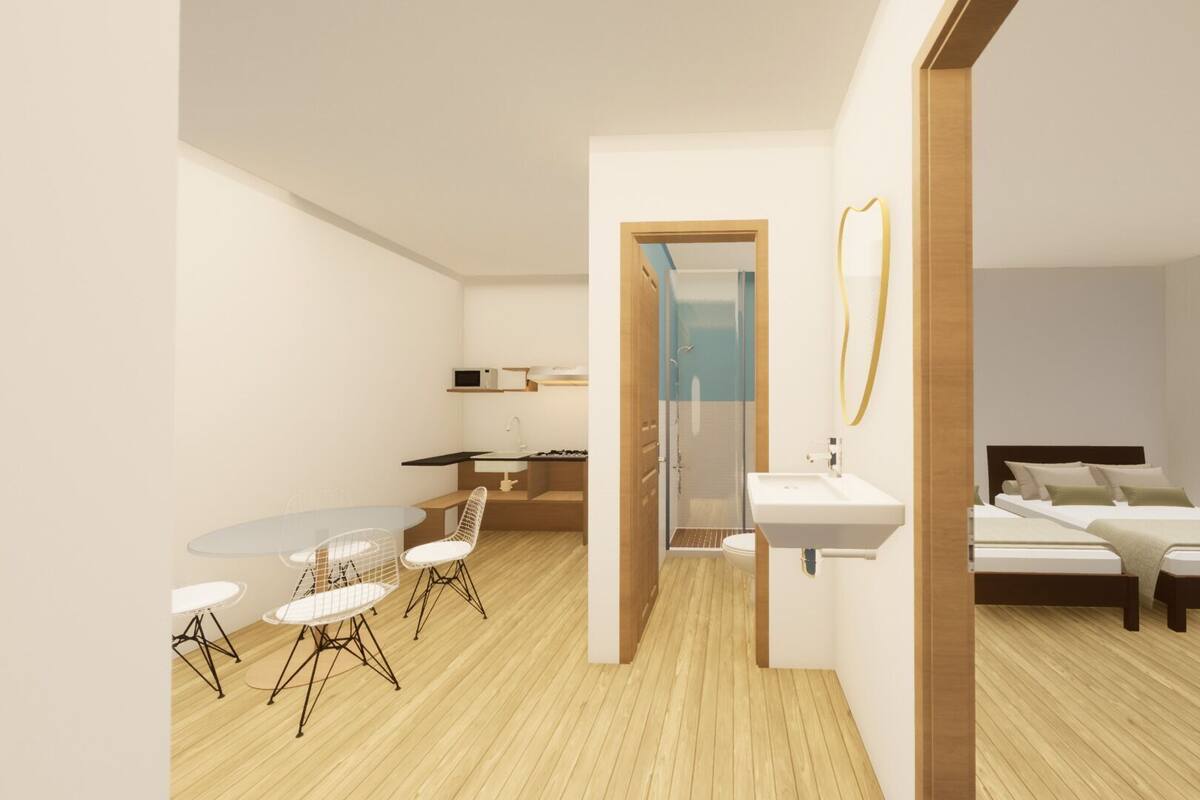 A modern hotel room with a wooden floor, a bed, a bathroom with a shower, and a dining area with a table and chairs.