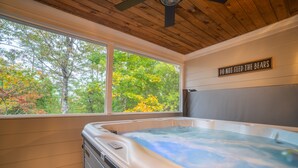A hot tub in a room with wooden ceiling and walls, a window with a view of trees, and a sign that says "DO NOT FEED THE BEARS".