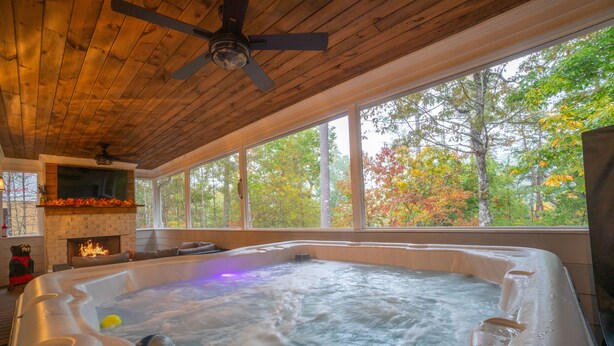 A hot tub with a wooden ceiling and large windows overlooking a forest.