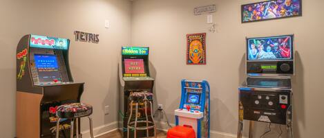 Ein Raum mit vier Spielautomaten, einem kleinen roten Hocker und einem Star Wars Poster an der Wand.