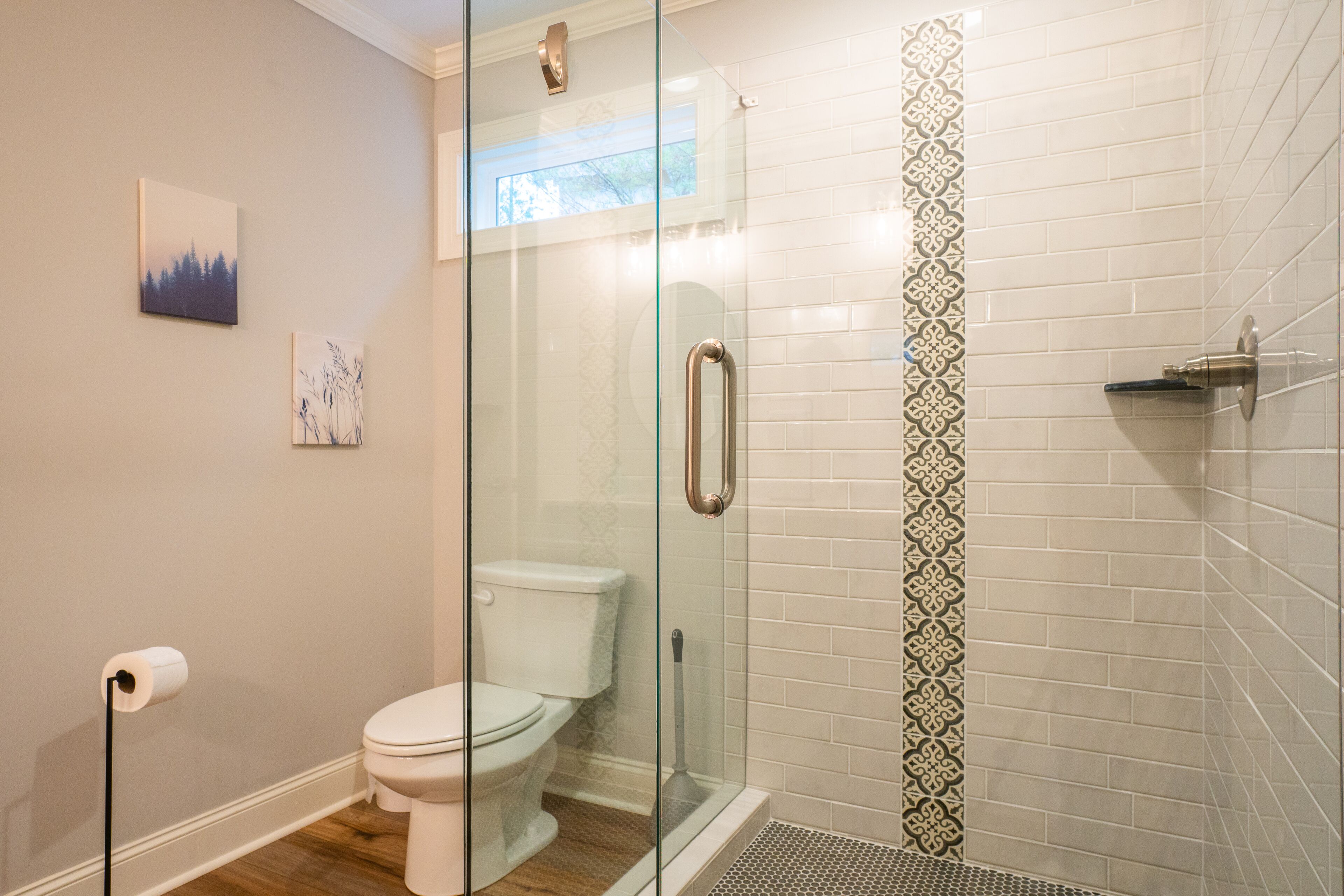 A bathroom with a glass-enclosed shower, a toilet, and a patterned tile backsplash.
