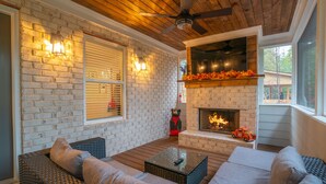 A cozy outdoor seating area with a brick fireplace, a ceiling fan, and a view of the outdoors.