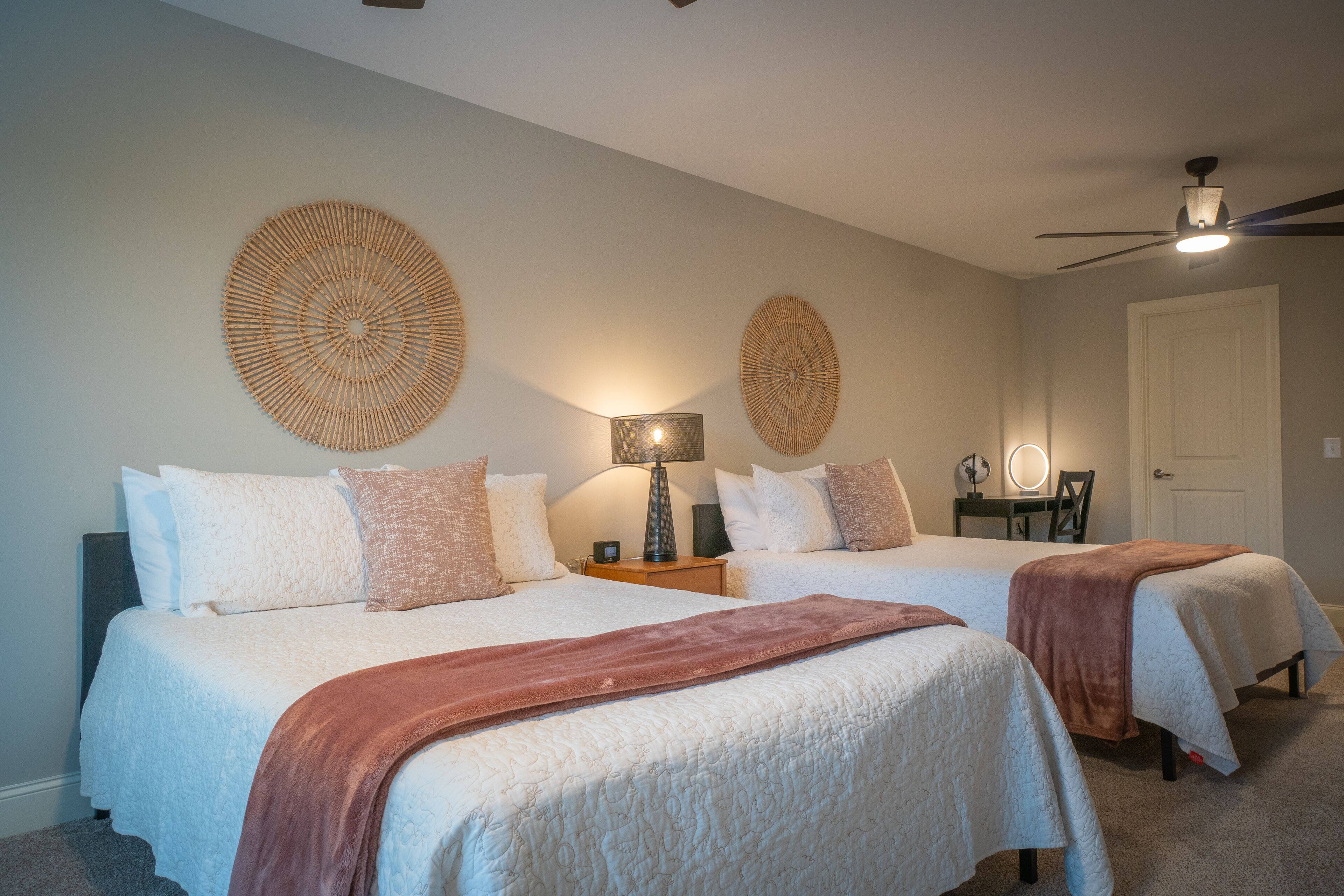 A bedroom with two beds, a ceiling fan, and wall decor.