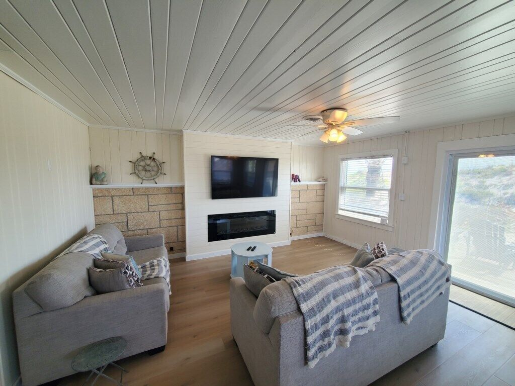A modern living room with two sofas, a flat-screen TV, a fireplace, and a ceiling fan.