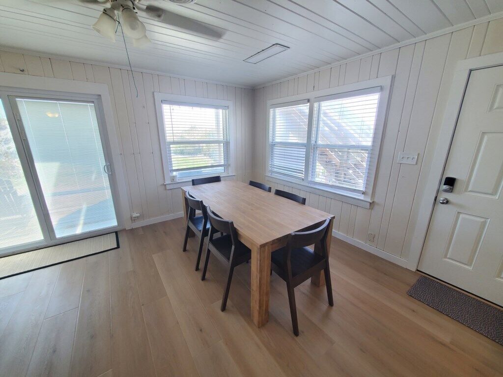Comedor con mesa y sillas de madera, ventanas amplias con persianas y un ventilador de techo.