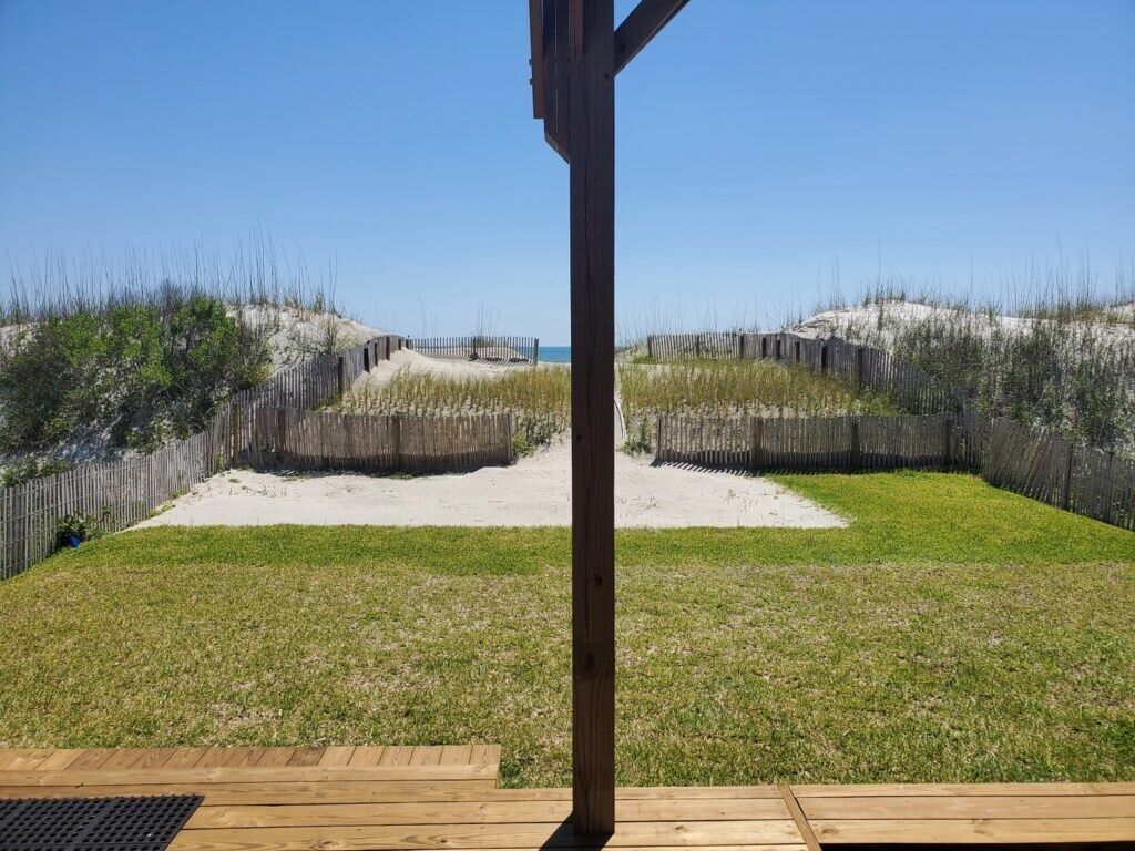 Ein Strandabschnitt mit Sand, einer Holzterrasse und einem Holzzaun.