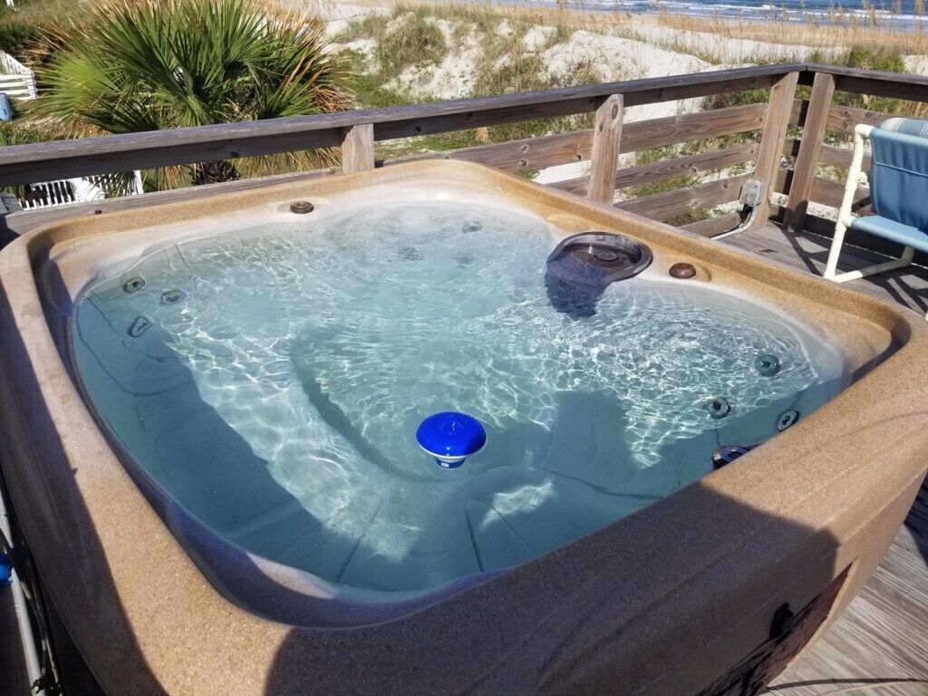 A hot tub on a wooden deck with a clear view of the beach in the background.