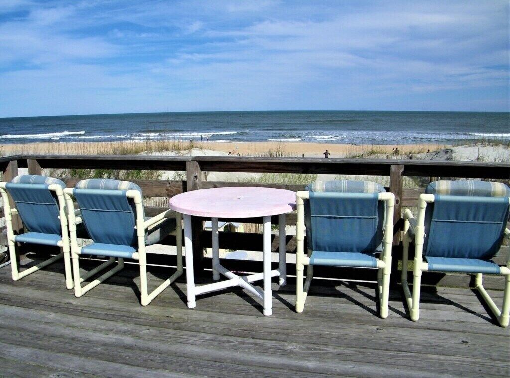 A deck with four blue chairs and a pink table, overlooking the beach.