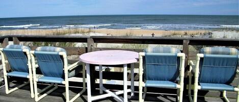 A deck with four blue chairs and a pink table, overlooking the beach.