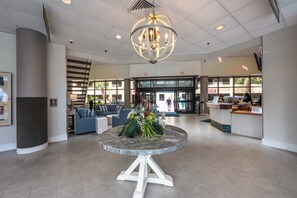 A lobby with a round marble table, blue sofas, a chandelier, and a reception desk. - Oceanfront condo with pool & beach access (North Myrtle Beach)